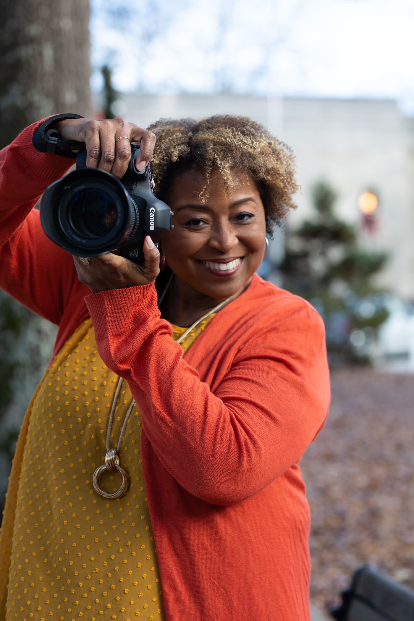 black female with camera wearing gold and orange